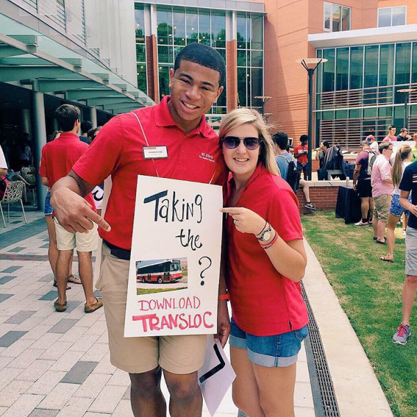 Student and TransLoc employee in front of a college campus holding a sign that reads Download TransLoc
