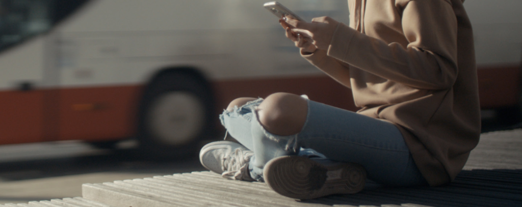 young woman looking at cell phone as a bus passes by