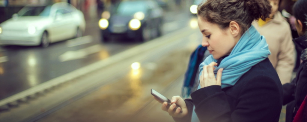 young woman looking at phone while waiting for a bus