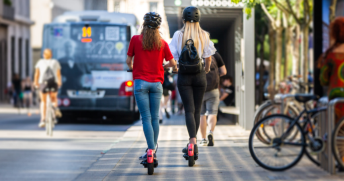 two young women using scooters on a city street
