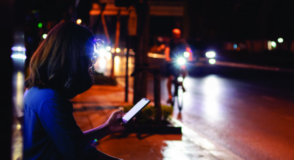 Woman sitting at a bus stop in the dark looking at her phone with a bicyclist approaching