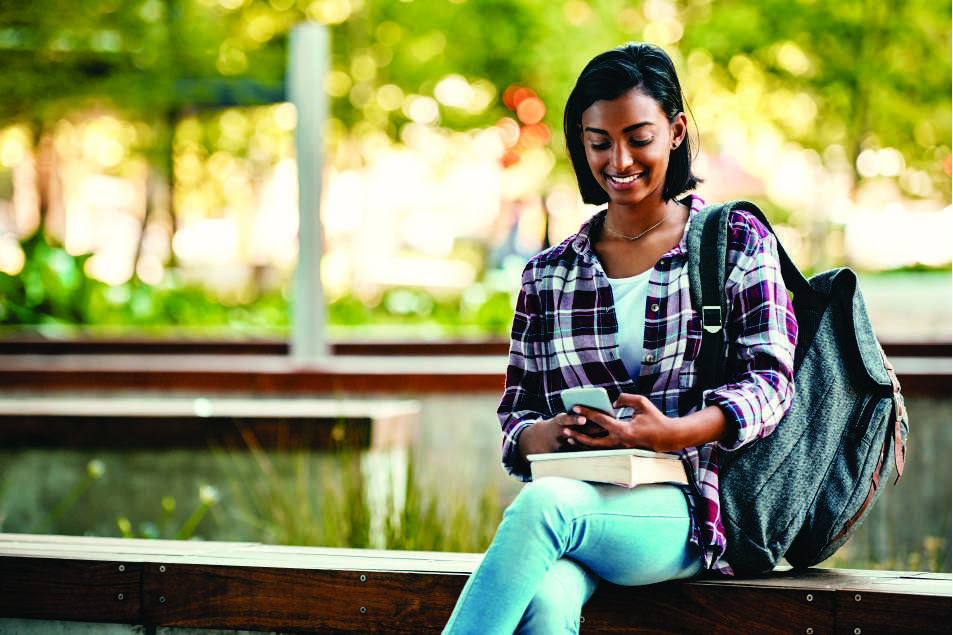 Female college student sitting on a bench with a backpack and cell phone